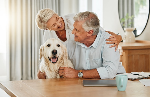 A happy senior couple sitting at a table with their golden retriever, symbolizing homeownership and estate planning.